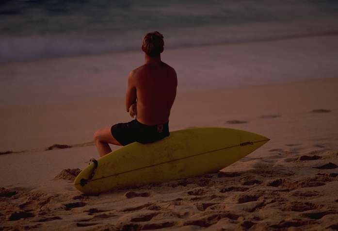 Surfista sentando en la tabla de surf en la arena